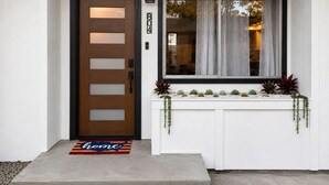A modern house entrance with a wooden door, a window with curtains, a mailbox, and a doormat. - Crater Lake Themed Retreat in Eagle Point (Eagle Point)