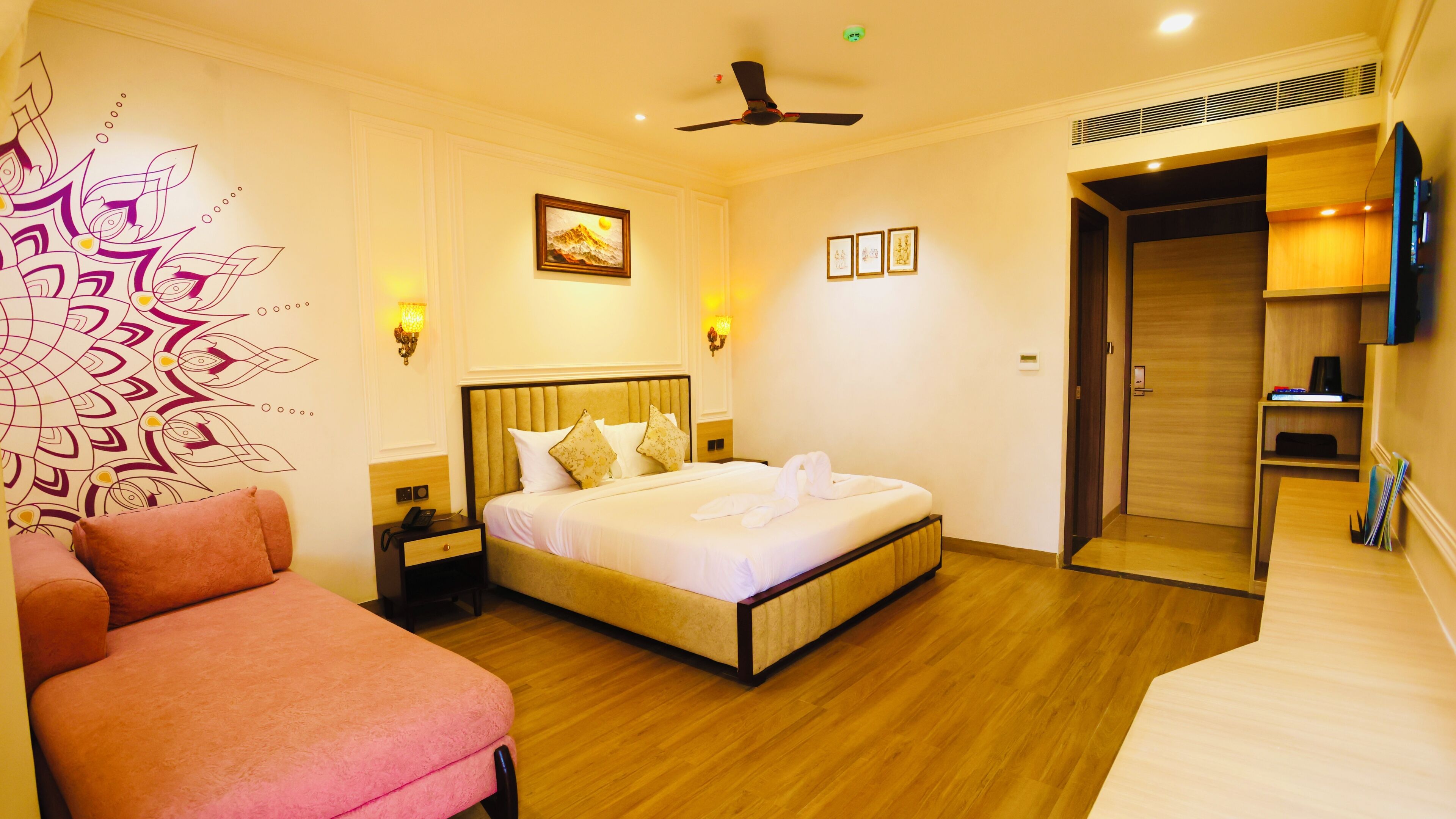 Una habitación de hotel con una cama, mesitas de noche, una silla, un ventilador de techo y una puerta que da a otra habitación.