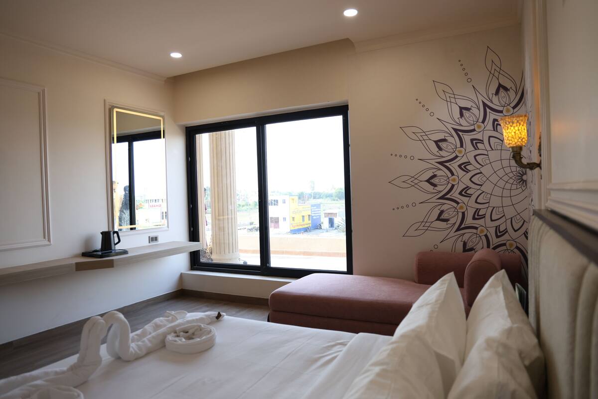Una habitación de hotel con una cama, un ventanal con vistas, una pared con un diseño decorativo y una mesita de noche con una lámpara.