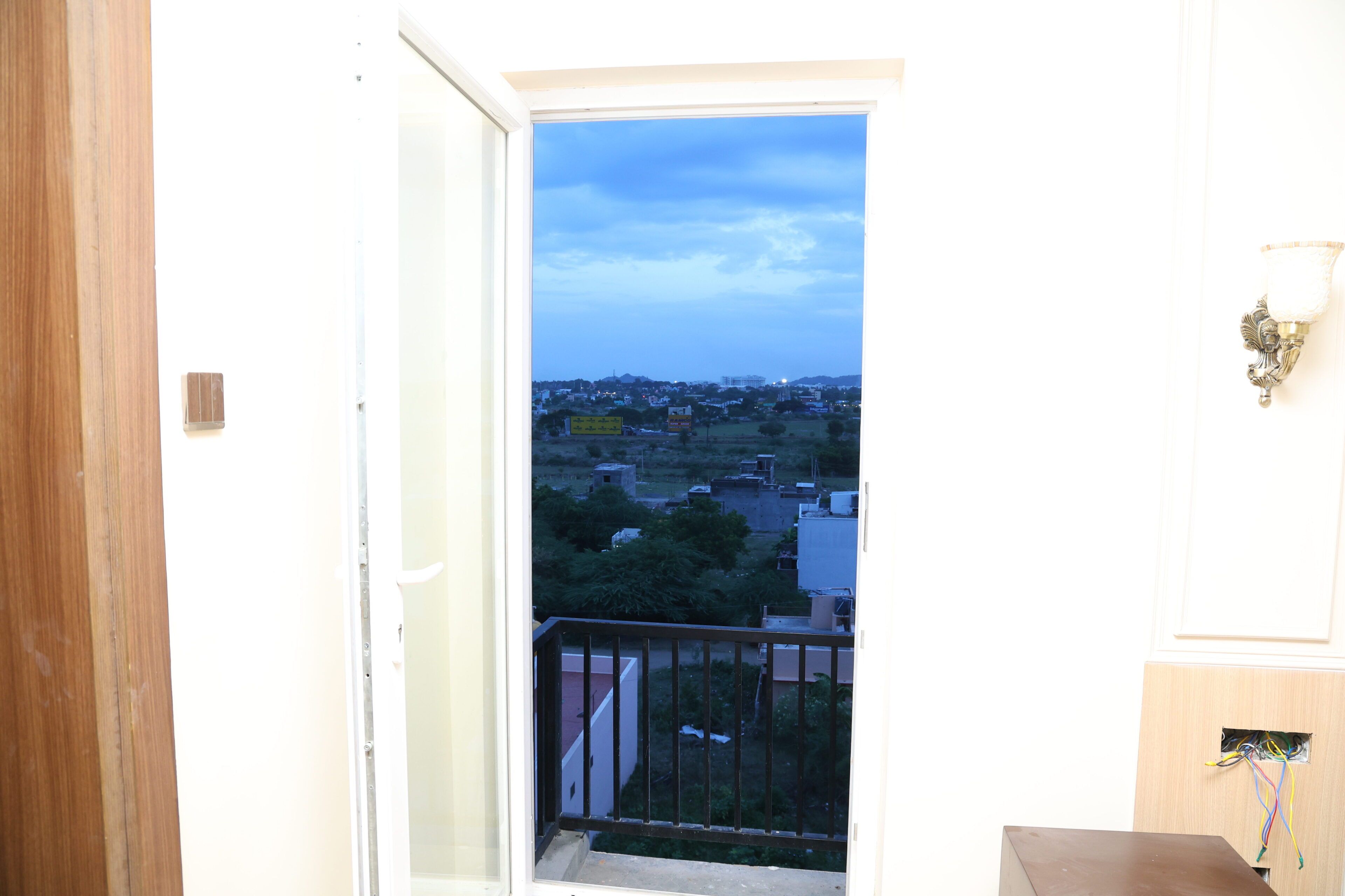 Un balcon donnant sur un quartier résidentiel, un luminaire fixé au mur et un cadre de porte.
