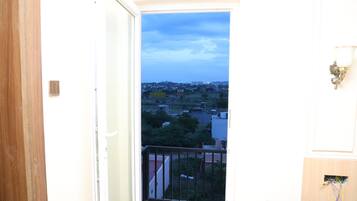 Un balcon donnant sur un quartier résidentiel, un luminaire fixé au mur et un cadre de porte.