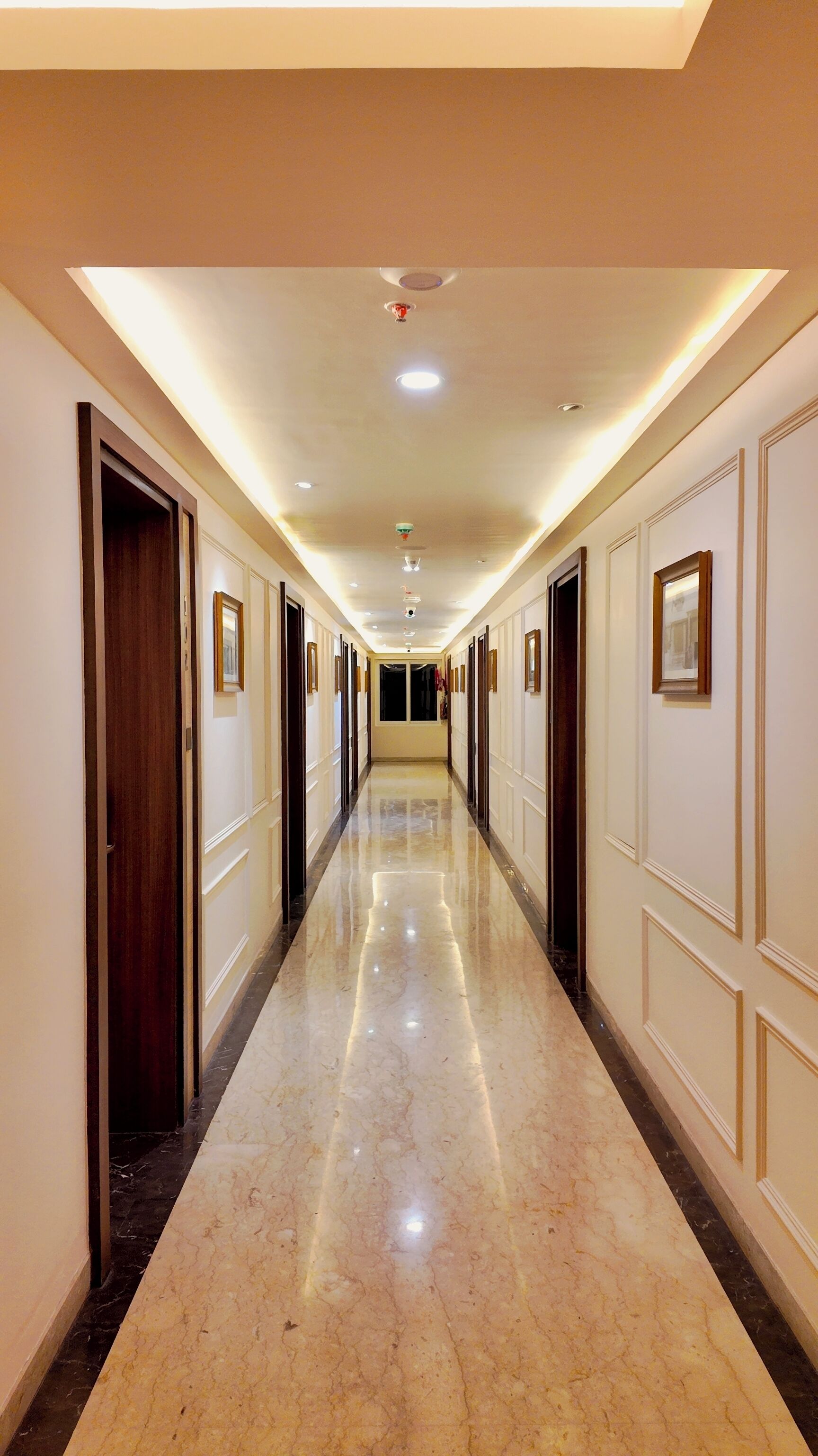 A long, well-lit hallway with doors on both sides, leading to rooms.