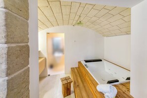 Een kamer met een houten bank, een witte badkuip en een bakstenen plafond.