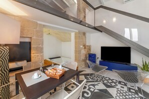 Ein modernes Wohnzimmer mit Kamin aus Stein, einem Flachbildfernseher, einem Esstisch mit Stühlen und einem gemusterten Boden.