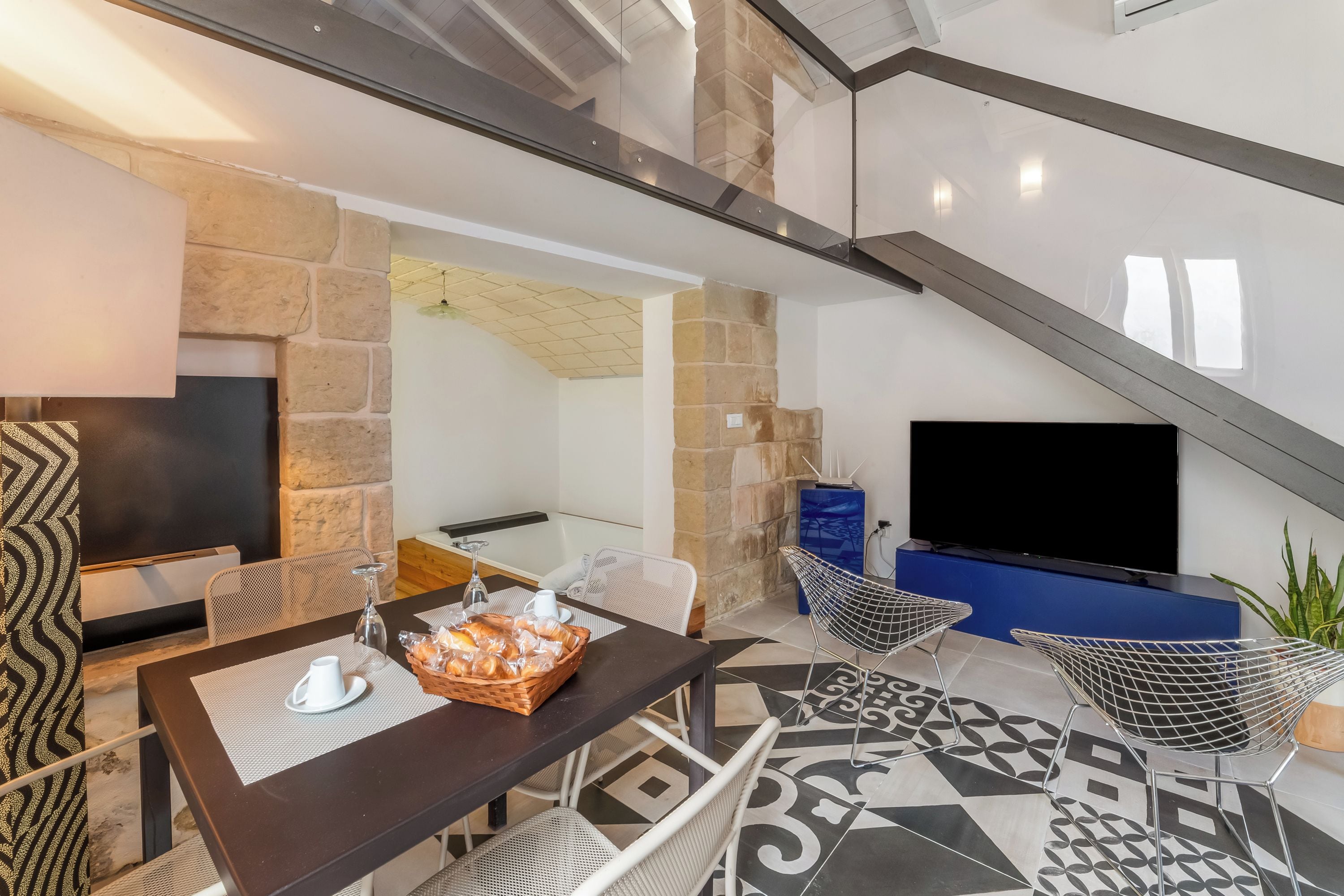 Ein modernes Wohnzimmer mit Kamin aus Stein, einem Flachbildfernseher, einem Esstisch mit Stühlen und einem gemusterten Boden.
