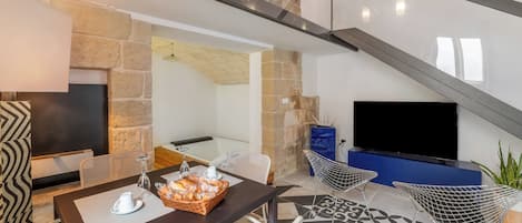 A modern living area with a stone fireplace, a flat-screen TV, a dining table with chairs, and a patterned floor.