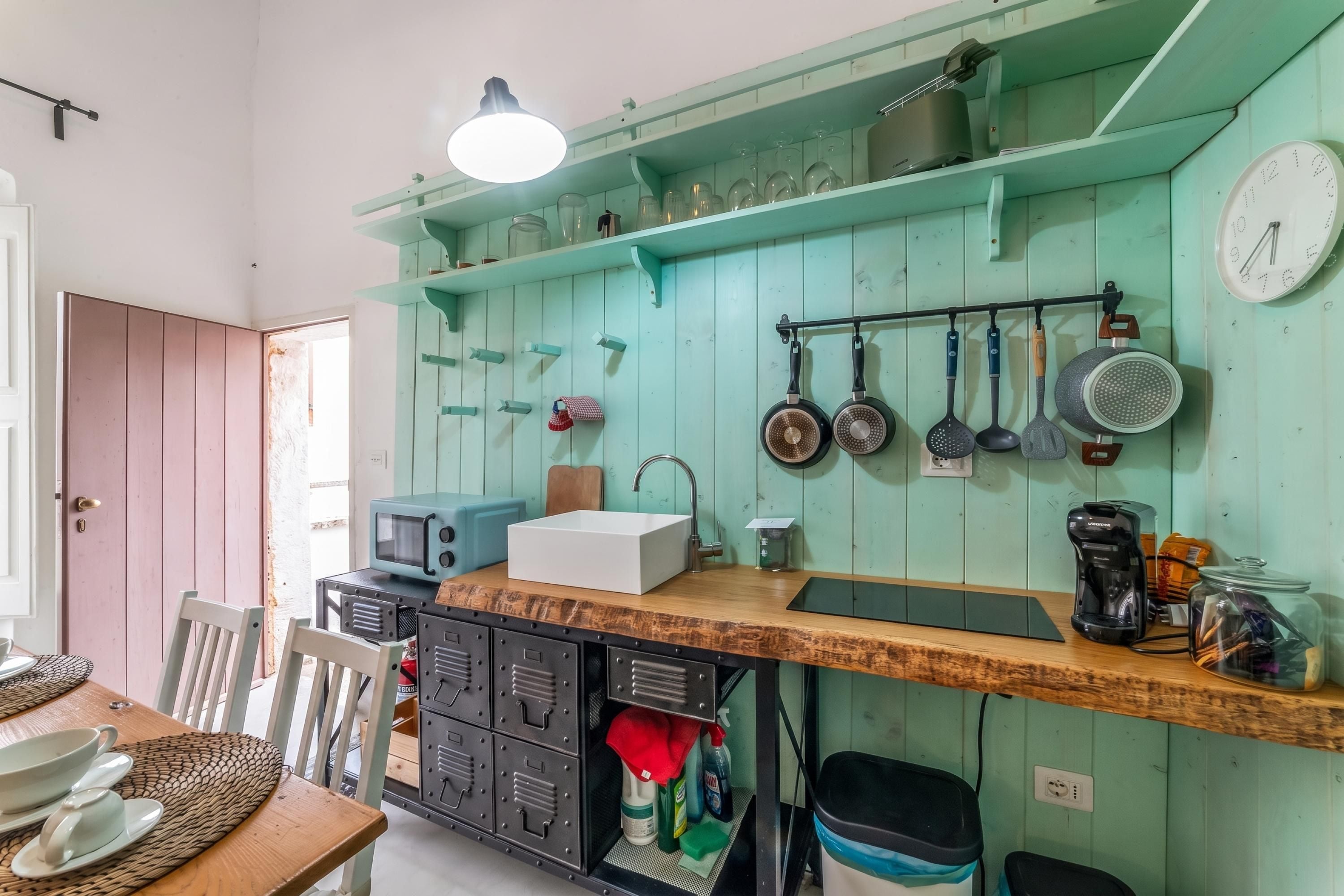 A kitchen with a wooden countertop, a sink, a microwave, and various utensils hanging on the wall.