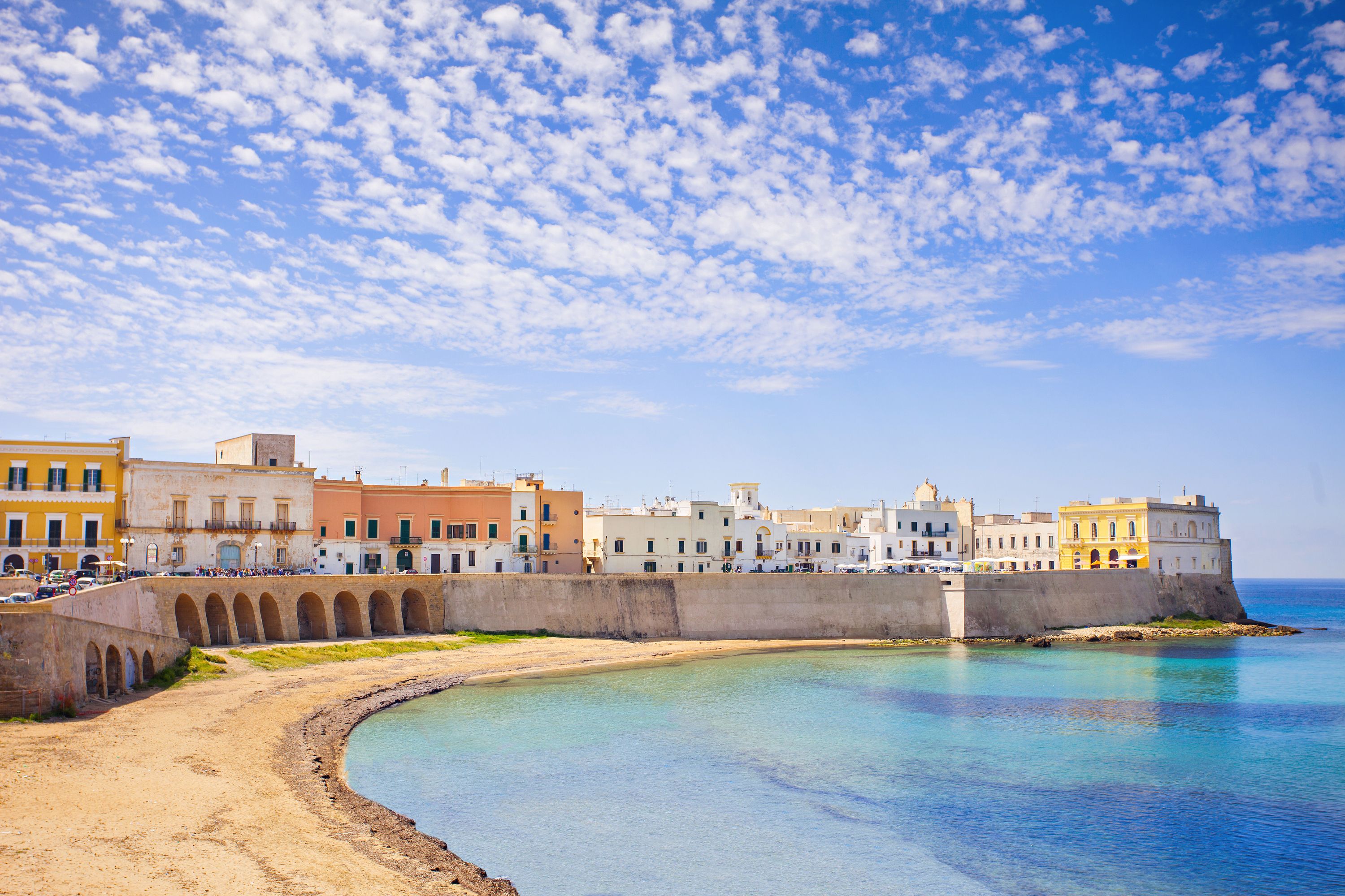 A coastal town with a curved waterfront, historic buildings, and a prominent fortification.
