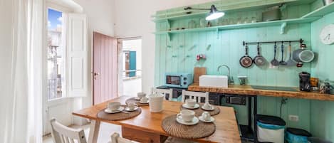 A kitchen with a wooden table set for four, white chairs, a teal backsplash, and various kitchen utensils.