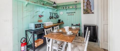 Cocina compacta con paredes color turquesa, una mesa de comedor de madera, sillas blancas y un refrigerador negro.