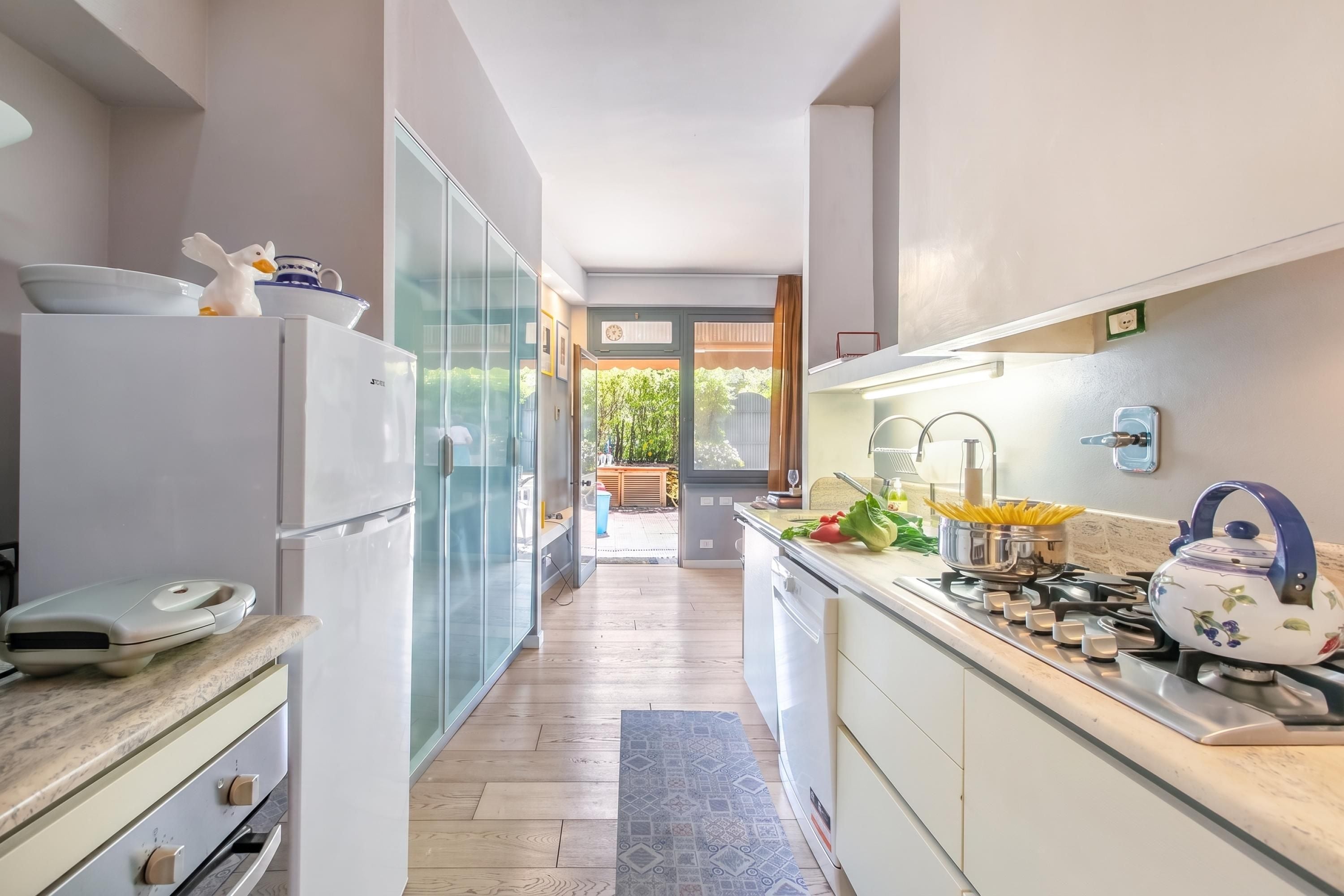 A modern kitchen with a refrigerator, oven, and stove. There is a window providing natural light and a view of the outdoors.