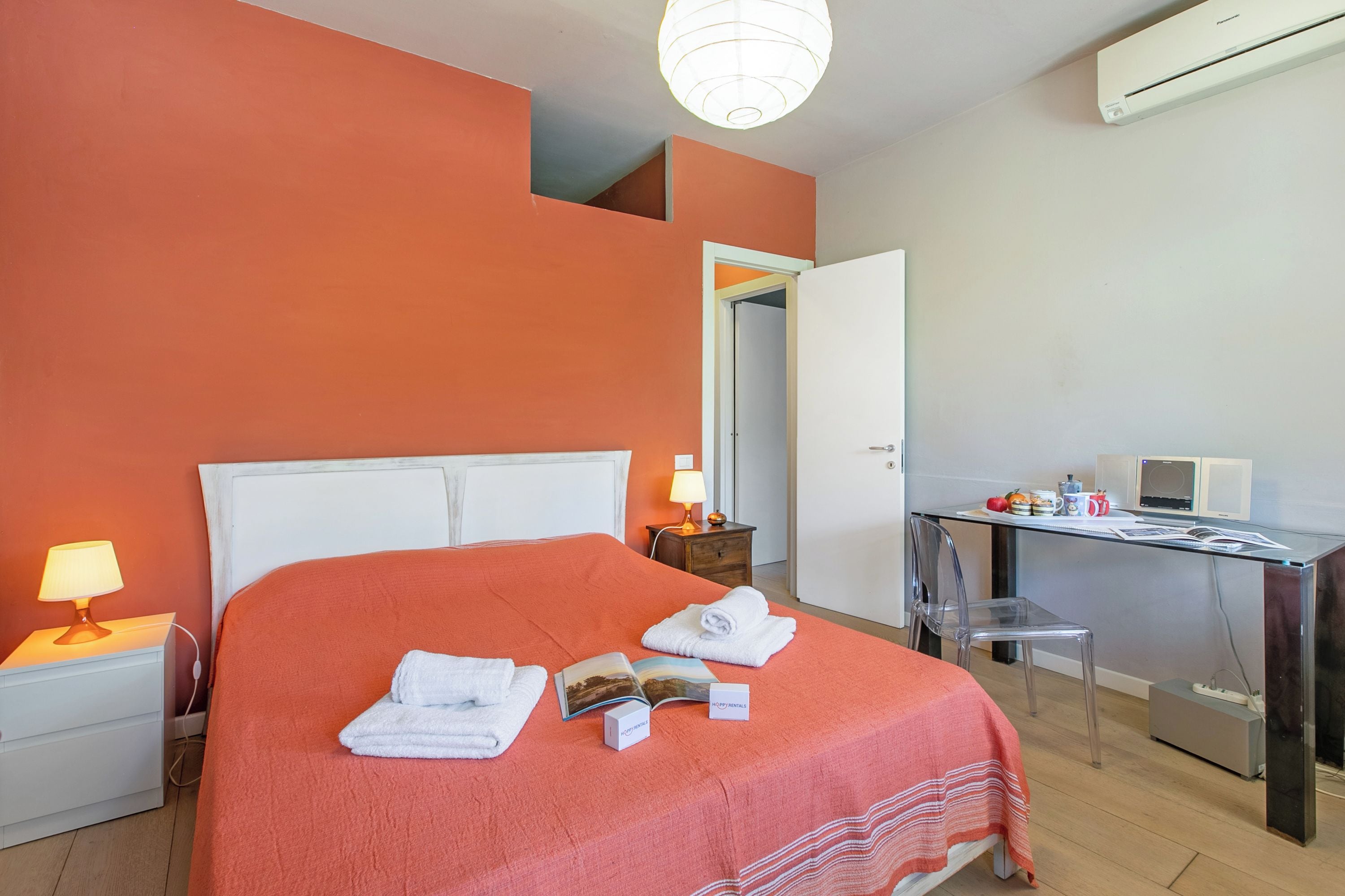 Una camera d'hotel con un letto, una scrivania, una sedia, una lampada e un condizionatore d'aria.