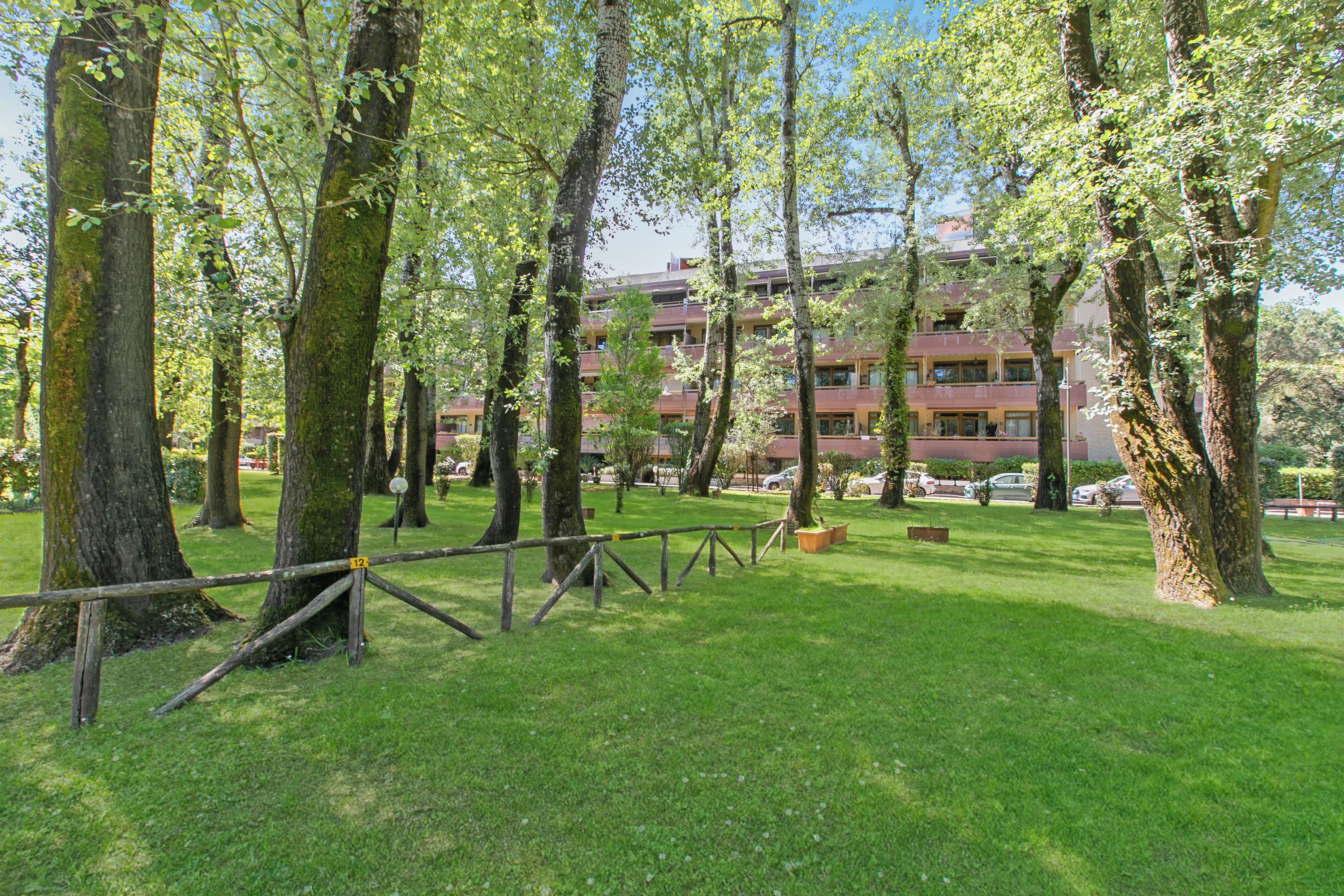 Un espacio verde con árboles y un edificio al fondo que tiene varios balcones.