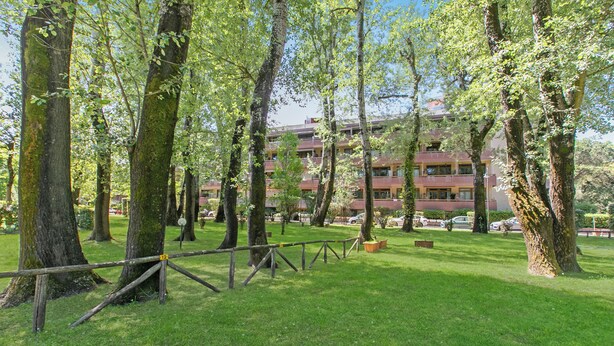 Ett grönområde med träd och en byggnad med flera balkonger i bakgrunden.