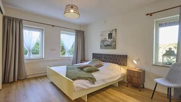 A bedroom with a bed, bedside table, chair, and a hanging light fixture.