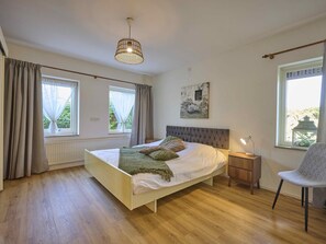 A bedroom with a bed, bedside table, chair, and a hanging light fixture.