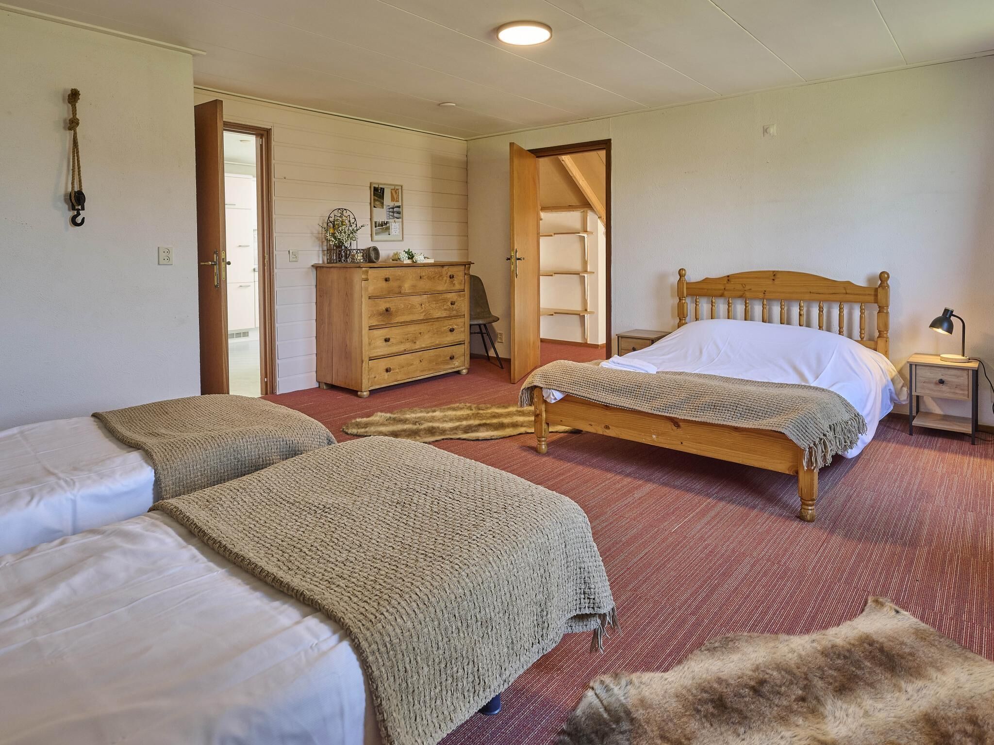 Een kamer met twee bedden, een houten dressoir, een nachtkastje en een deur naar een andere kamer.