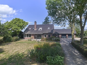 A two-story house with a brick exterior, a tiled roof, and a front porch with a bench.