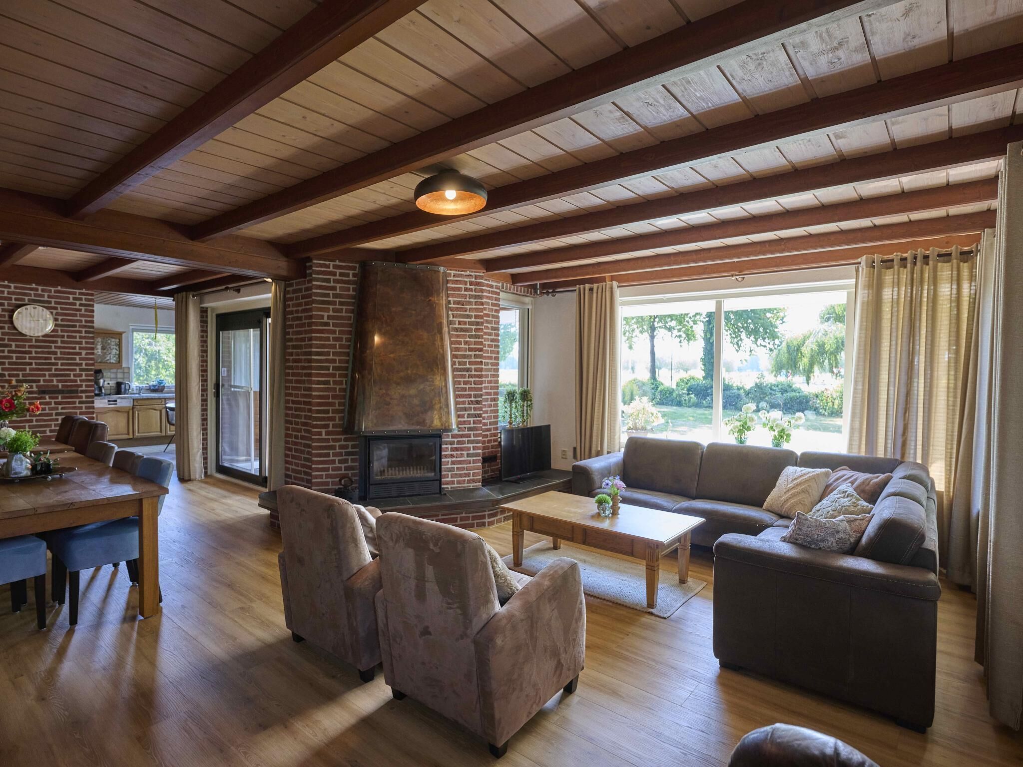 A spacious living room with a fireplace, a sofa, a coffee table, and a dining area with a brick wall and a window.
