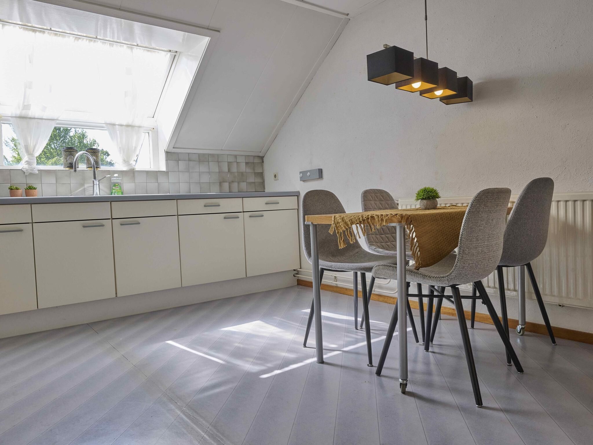 Een moderne keuken met een eethoek, voorzien van een dakvenster, witte kasten en een tafel met stoelen.