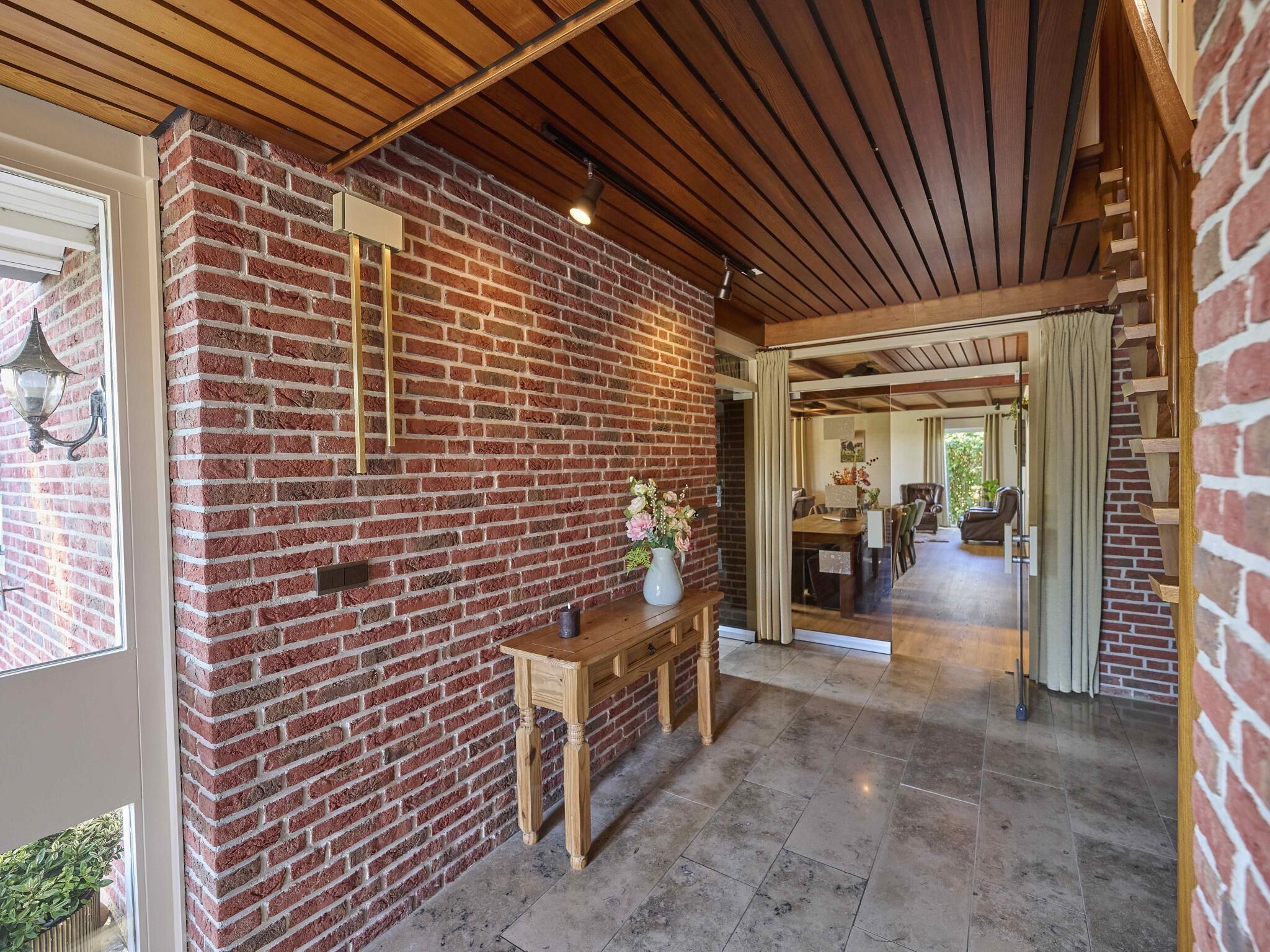 A hallway with a brick wall, wooden ceiling, and a bench with a vase.