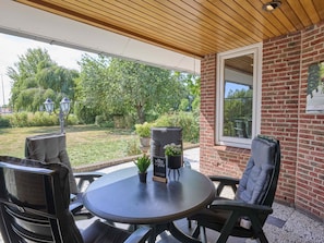 An outdoor patio with a round table, two chairs, a potted plant, and a sign.