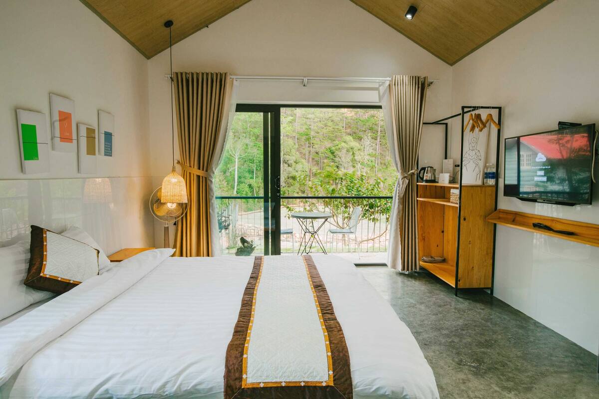 A bedroom with a bed, a TV, a desk, and a view of the outdoors.