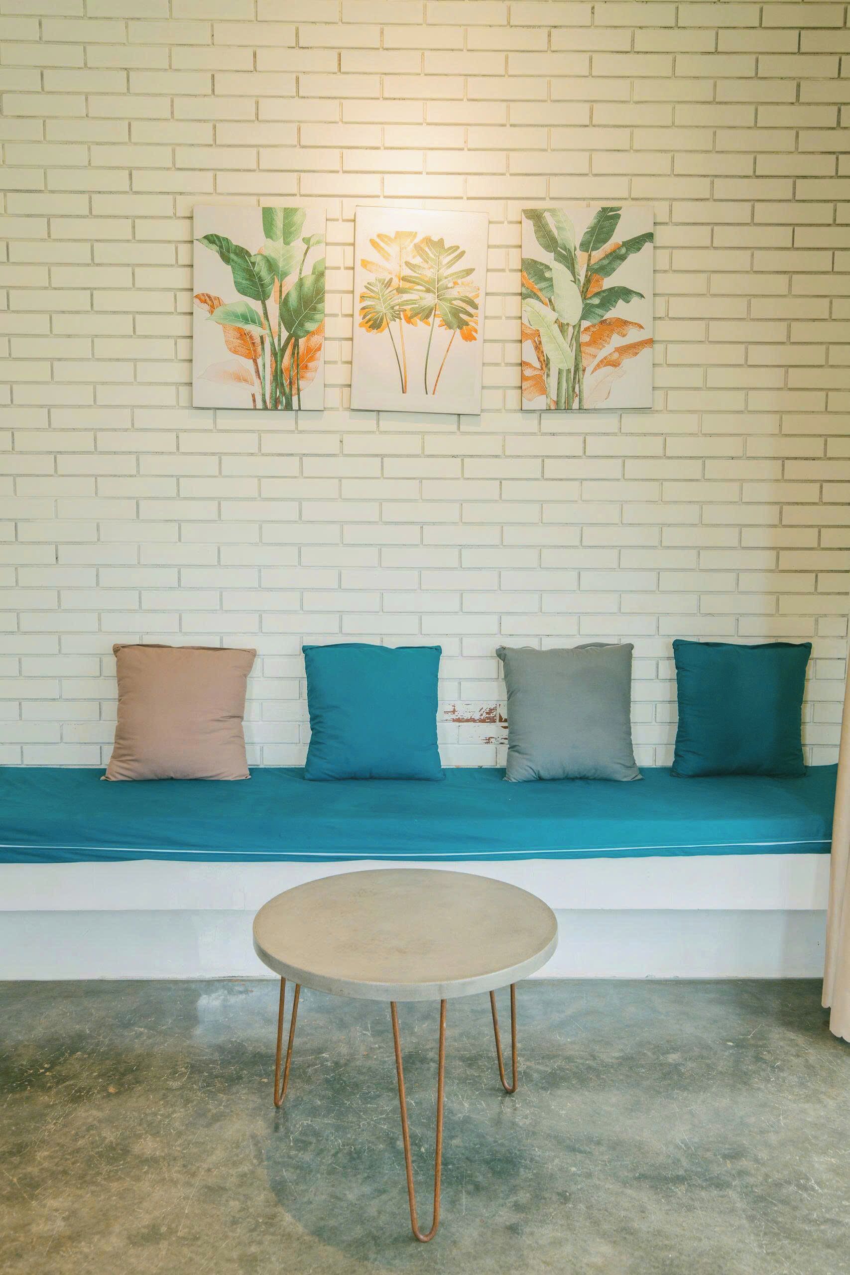 A room with a white brick wall, a teal sofa with cushions, and a round table with metal legs.
