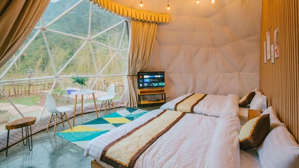 A bedroom with a large window, a bed, a TV, and a small table with chairs.