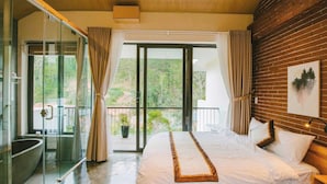 A bedroom with a large bed, a glass shower enclosure, and a balcony with a view.