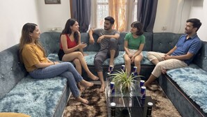 Un grupo de personas sentadas en un sofá en una habitación con una mesa de vidrio y una planta.