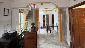 Un hall de hotel con mostrador de recepción, zona de estar, escalera y ventilador de techo.