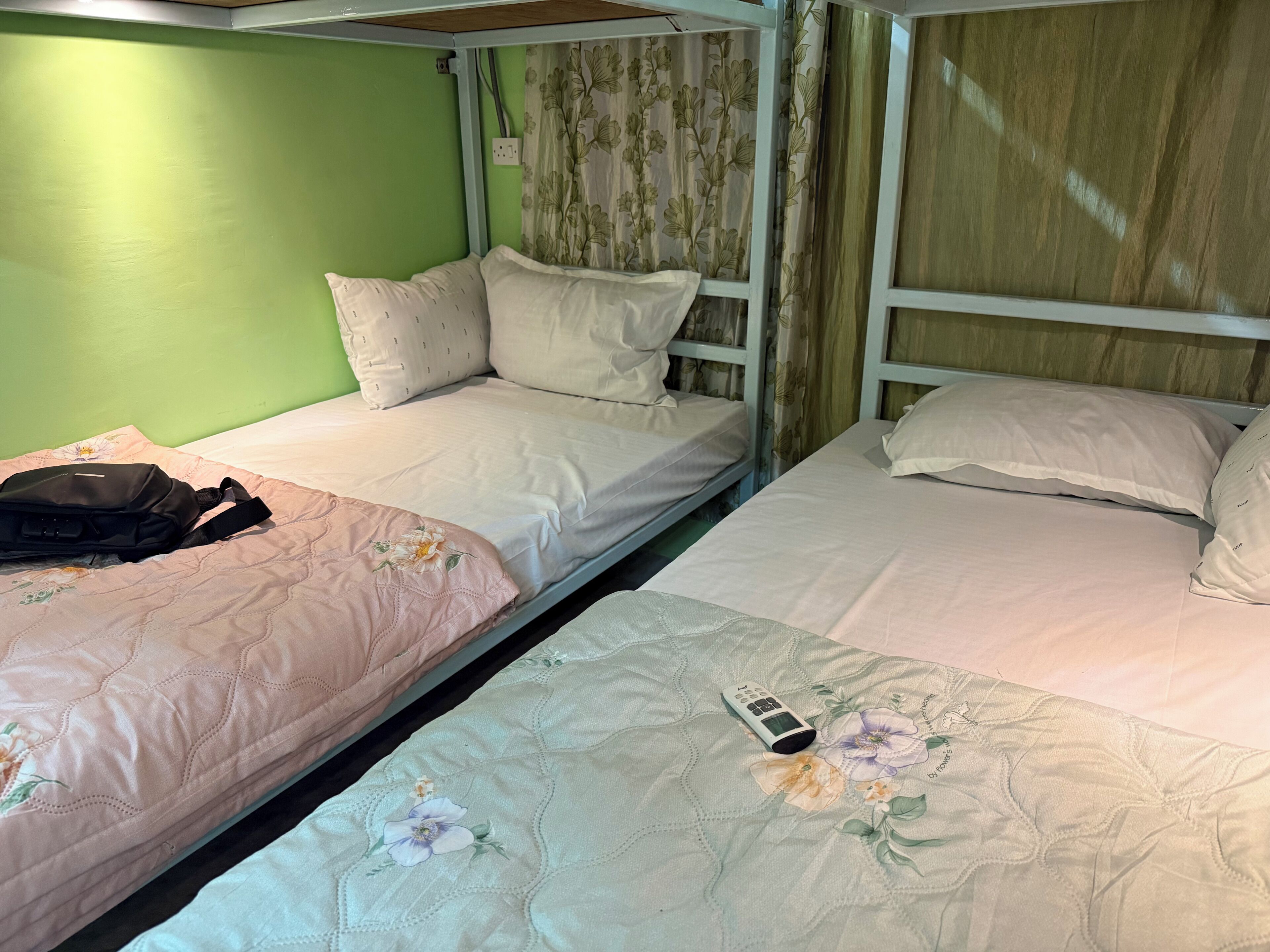 Une chambre avec un lit superposé, un mur vert, une literie à motifs floraux et une télécommande sur le lit du bas.