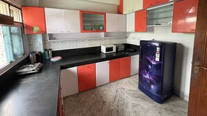 Una cocina con gabinetes rojo y blanco, una encimera negra, microondas, tostadora, refrigerador y estufa a gas.