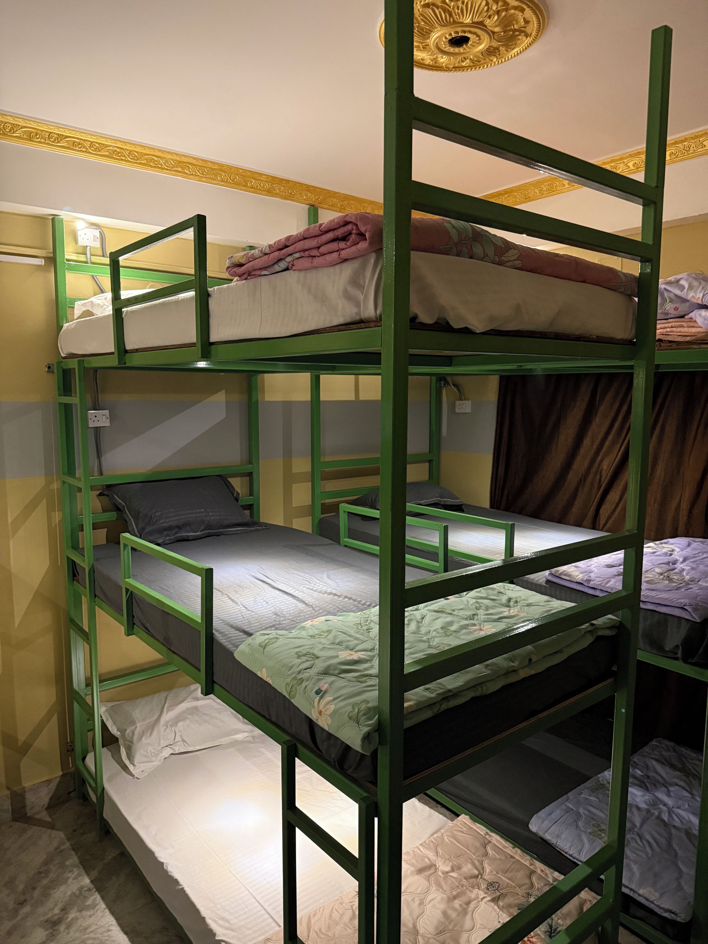 A bunk bed room with a green frame, a ceiling light fixture, and a plain wall.