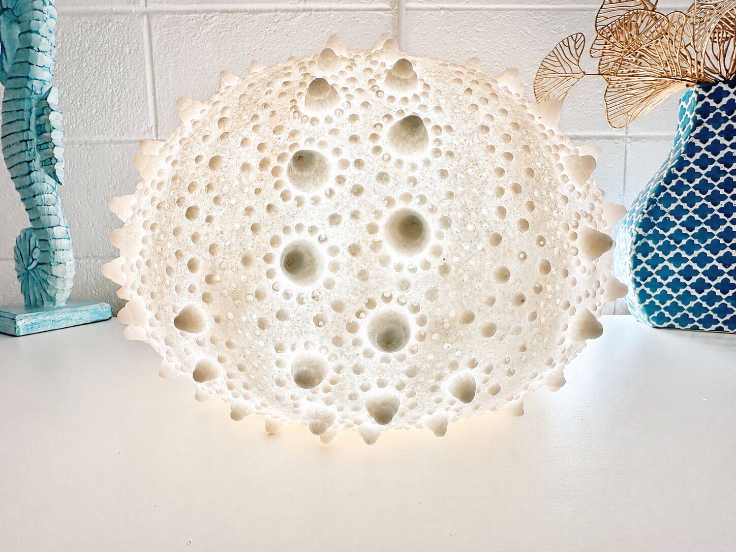 A textured spherical object with a porous surface, possibly a decorative piece, on a white surface.