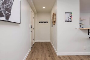 A hallway with a wooden floor, a coat rack, and a wall-mounted artwork. - Inlet View Luxe -King Suite - Downtown Anchorage (Anchorage)
