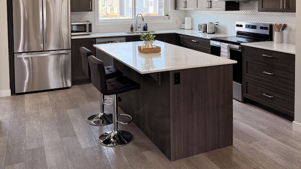 Una cocina moderna con gabinetes de madera oscura, electrodomésticos de acero inoxidable, una isla central con taburetes de bar, iluminación colgante y vistas al exterior.