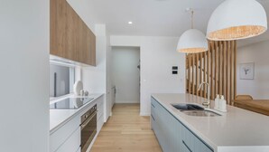 A modern kitchen with wooden cabinets, a central island with a sink, pendant lights, and a view into the dining area. - Offshore Escape - Welcome to your dream North Coast escape (Skennars Head)