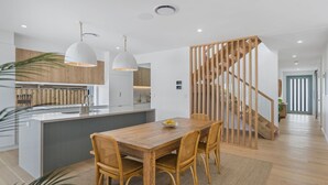 A modern kitchen with wooden cabinets, a central island, pendant lighting, and a staircase with wooden railings. - Offshore Escape - Welcome to your dream North Coast escape (Skennars Head)