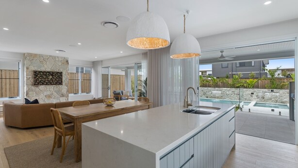 A modern kitchen with a central island, a dining area with a wooden table, and a view of a swimming pool. - Offshore Escape - Welcome to your dream North Coast escape (Skennars Head)
