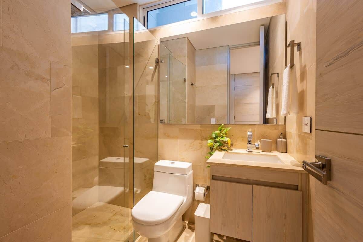 A modern bathroom with a glass shower enclosure, a toilet, a sink with a mirror, and wooden cabinetry.