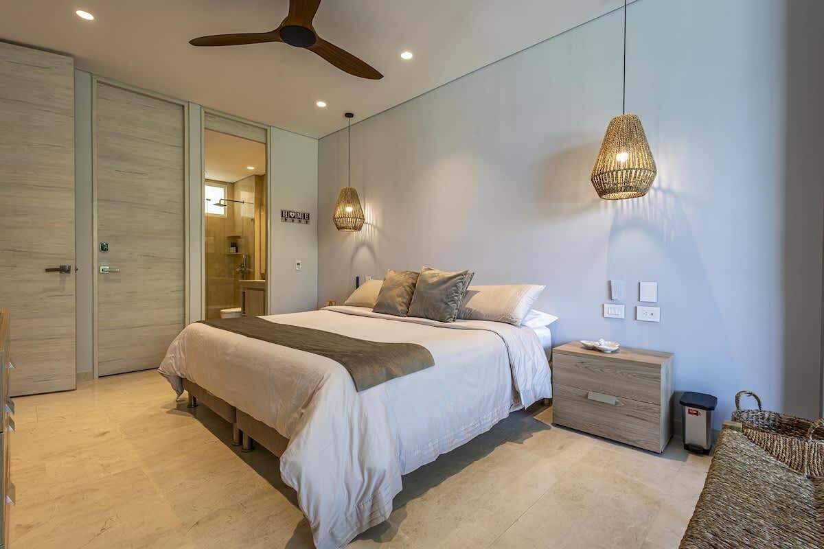 A modern bedroom with a large bed, a wooden nightstand, a woven basket, and a ceiling fan.
