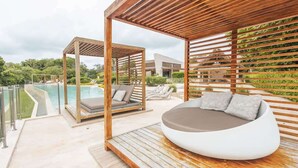 A modern outdoor lounge area with a pool, wooden pergola, and a unique seating pod. - Apex Executive Apartments - Calablanca (Barú)