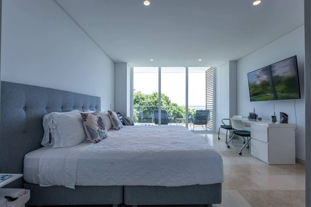 A modern bedroom with a large bed, a desk, and a TV.