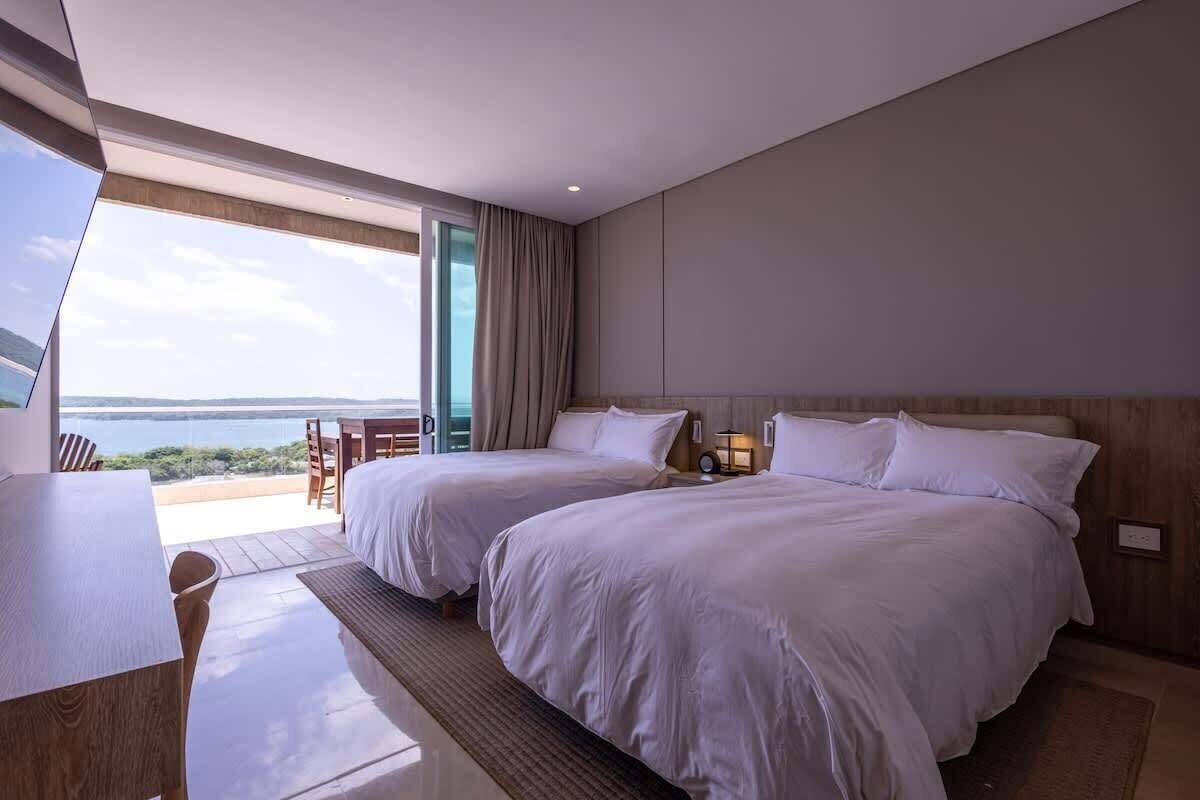 A hotel room with two beds, a dining table, and a view of the sea.