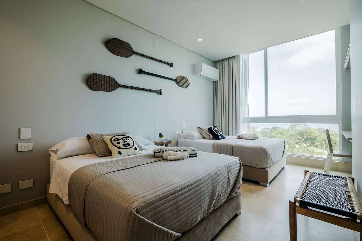A hotel room with two beds, a large window, and wall-mounted paddleboards.