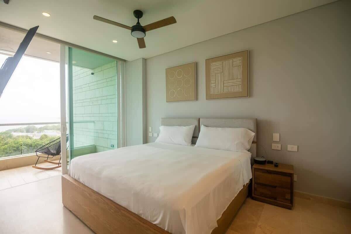 A bedroom with a bed, a nightstand, a ceiling fan, and a window with a view.