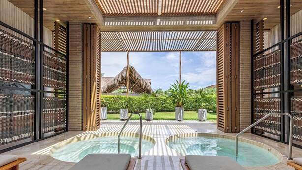 An indoor swimming pool with lounge chairs and a view of a thatched-roof structure. - Apex Executive Apartments - Calablanca (Barú)