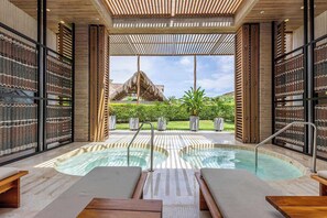 Une piscine intérieure dotée de chaises longues et offrant une vue sur une structure au toit de chaume.